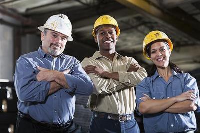 Three people are standing together, smiling, and wearing construction hard hats.