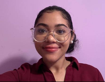 Prince George's Community College Student Lemoni Conde smiles at the camera wearing eyeglasses against a pink background.
