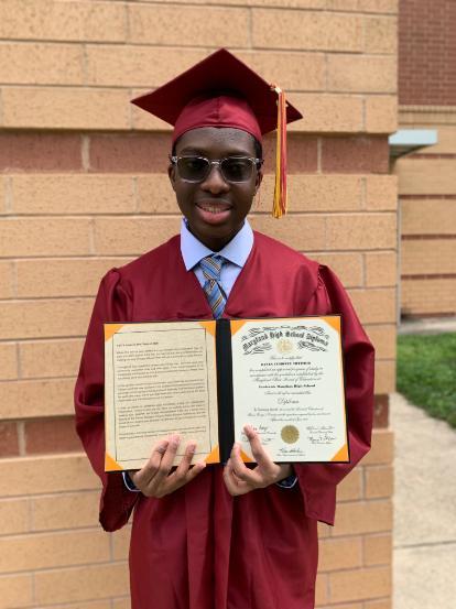 PGCC Student Kevin Totimeh, in a cardinal-colored cap and gown, smiling and holding his high school diploma.